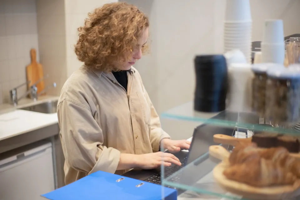 Eine Mitarbeiterin arbeitet hinter der Theke einer Bäckerei am Laptop