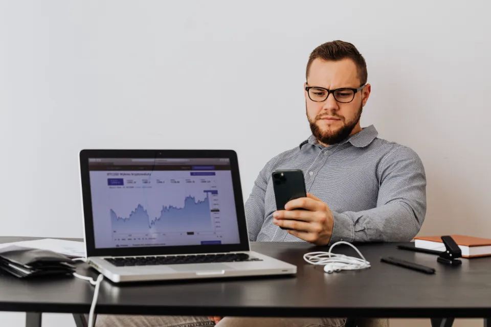 Ein Unternehmer prüft an seinem Schreibtisch Kennzahlen auf dem Laptop und dem Handy