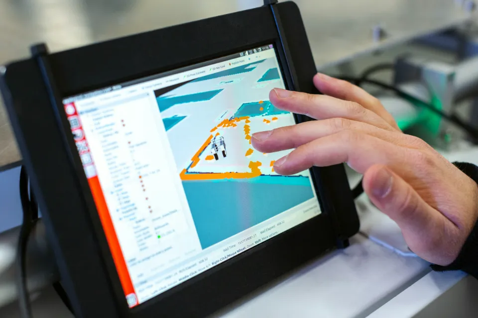 Eine Hand bedient auf einem Tablet in der Werkhalle eine Software für die Fertigung