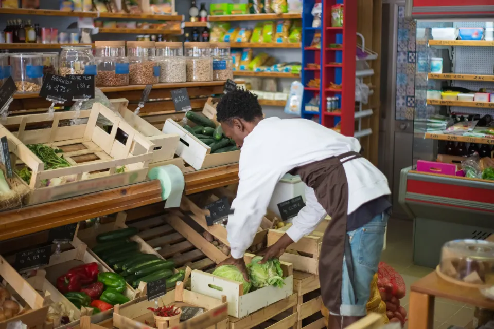 Ein Mitarbeiter prüft in einem kleinen Laden Salat und Gemüse von Hand
