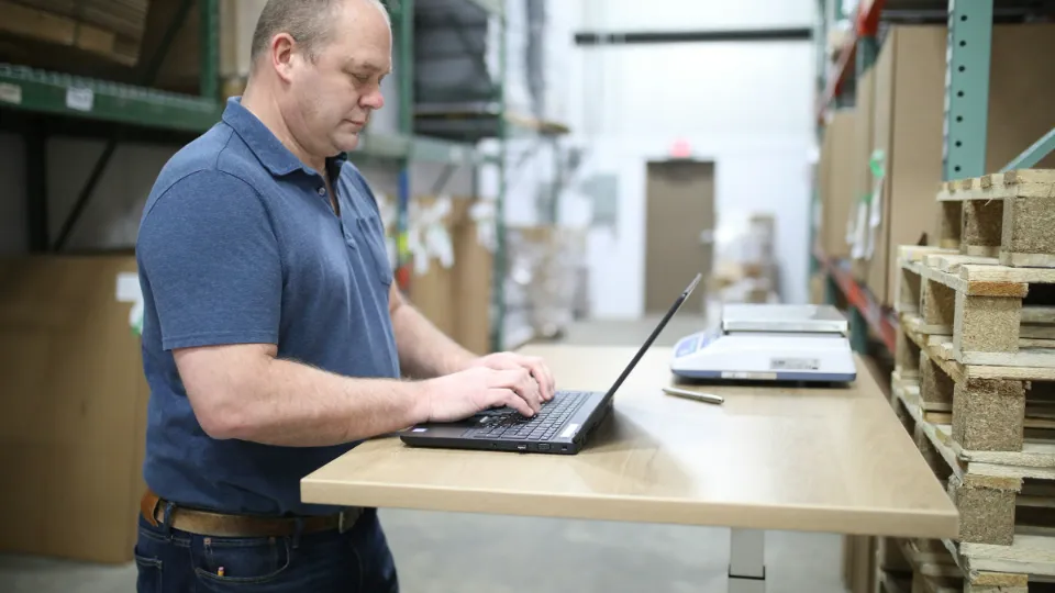 Ein Mitarbeiter arbeitet im Lager an einem Stehpult am Laptop