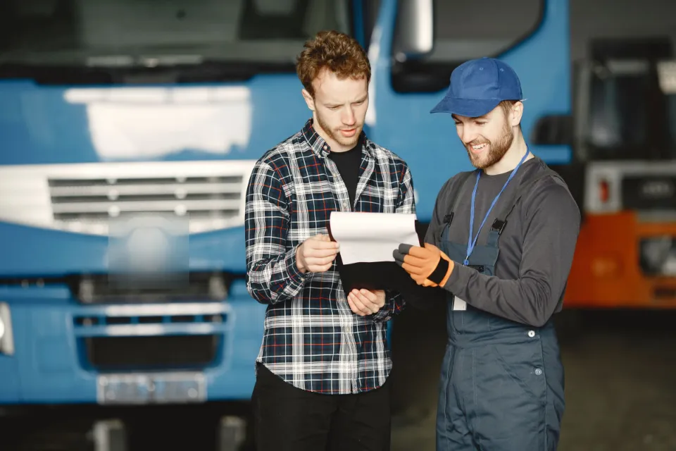 Ein Fahrer und ein Kollege besprechen vor einem Lkw die Lieferpapiere