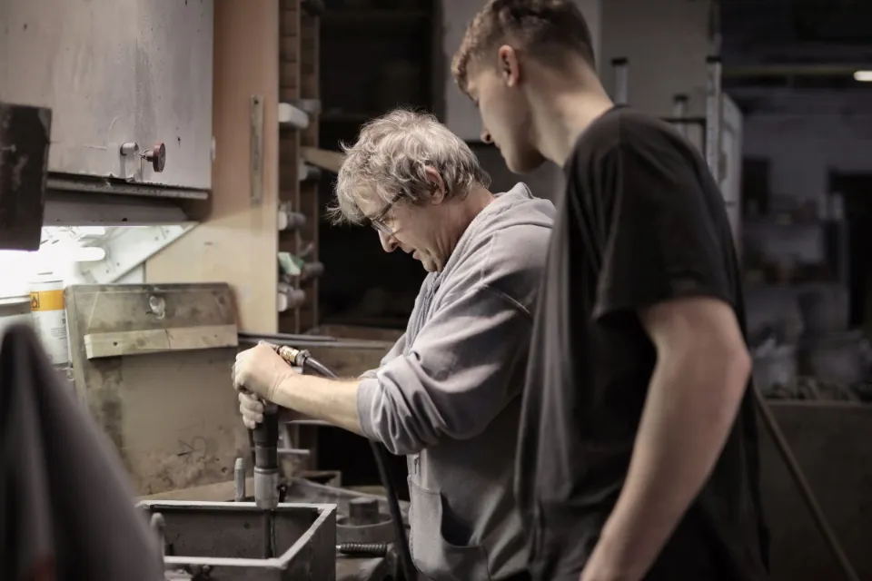 Ein erfahrener Metallbauer zeigt einem jungen Kollegen in der Werkstatt einen Arbeitsschritt