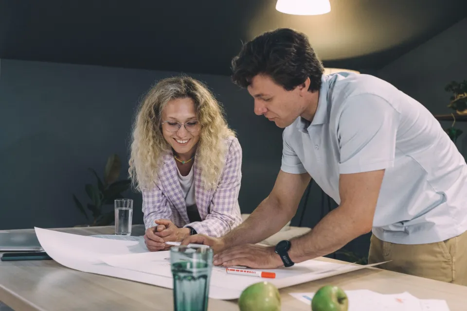 Eine Frau und ein Mann beugen sich gemeinsam über einen großen Plan auf dem Tisch und besprechen den nächsten Schritt