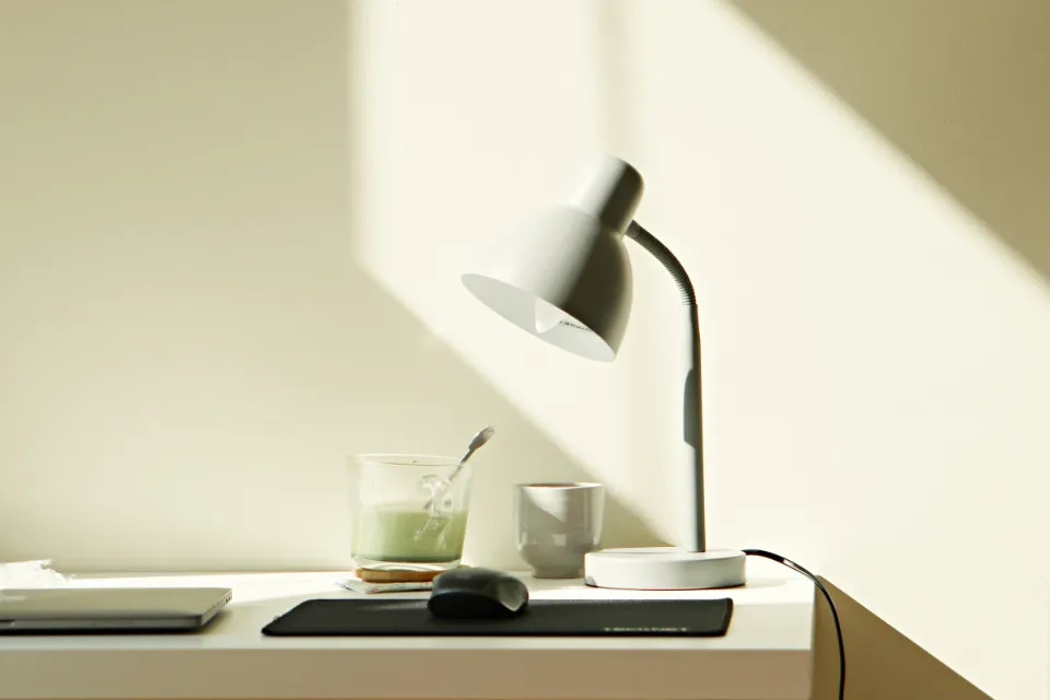 Ein aufgeräumter heller Schreibtisch mit Lampe und Tasse im Sonnenlicht