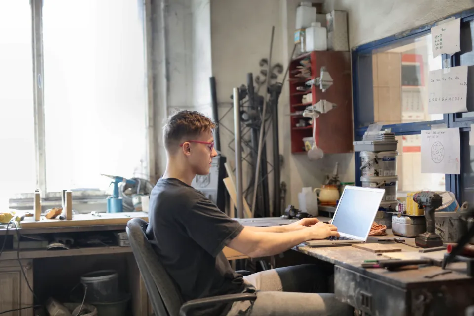 Ein junger Mann arbeitet in einer Werkstatt am Laptop
