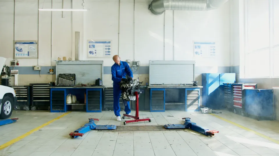 Ein Mechaniker arbeitet in einer hellen, aufgeräumten Werkstatthalle an einem Motor